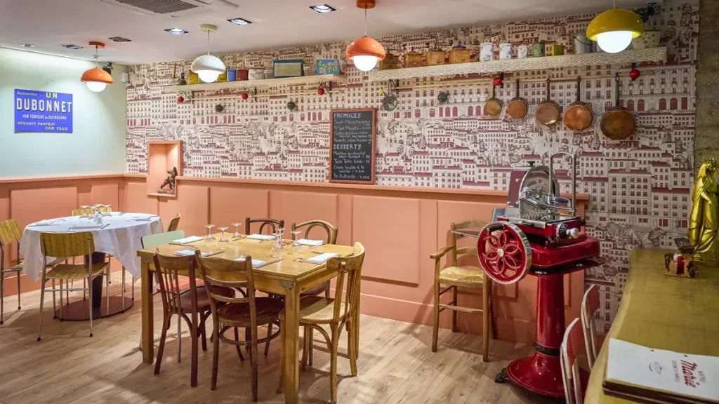 Salle intérieure du Bistrot Marie à Lyon, restaurant de cuisine traditionnelle lyonnaise situé rue du Bœuf dans le Vieux-Lyon. Décoration vintage avec objets chinés, papier peint illustré de Lyon, chaises bistrot en bois et luminaires colorés — une ambiance chaleureuse et authentique