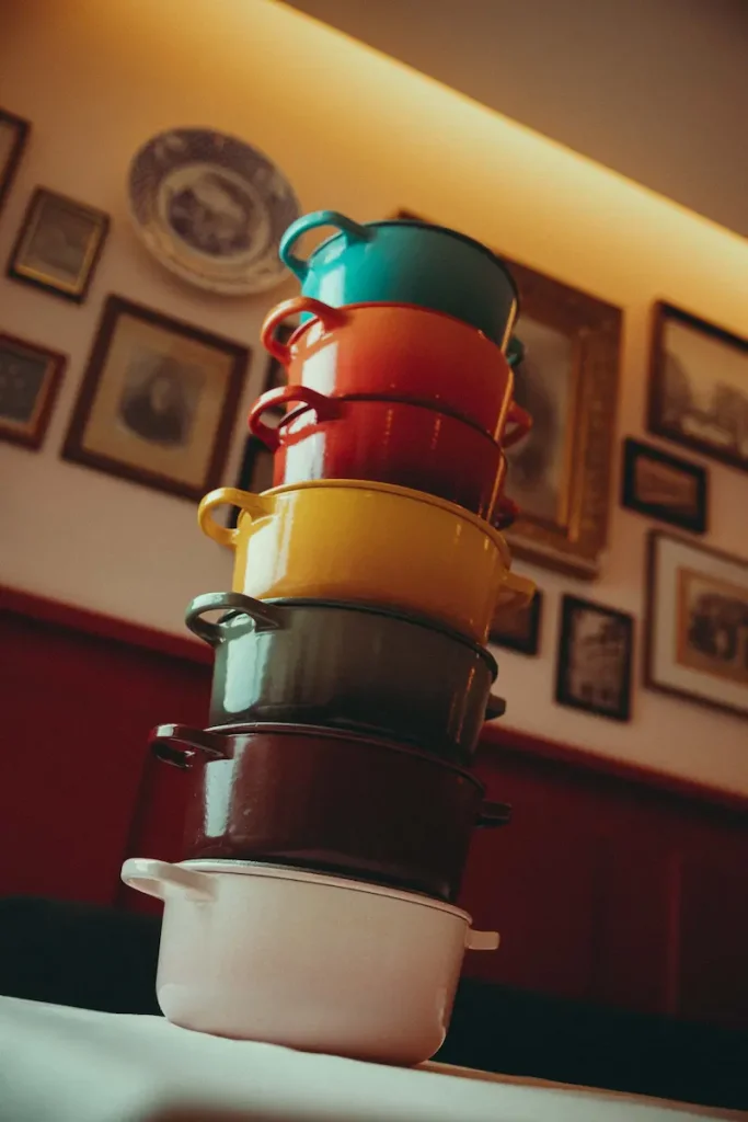 Pile de cocottes en fonte colorées sur une table devant les cadres anciens de la salle du Bistrot Marie, Vieux-Lyon