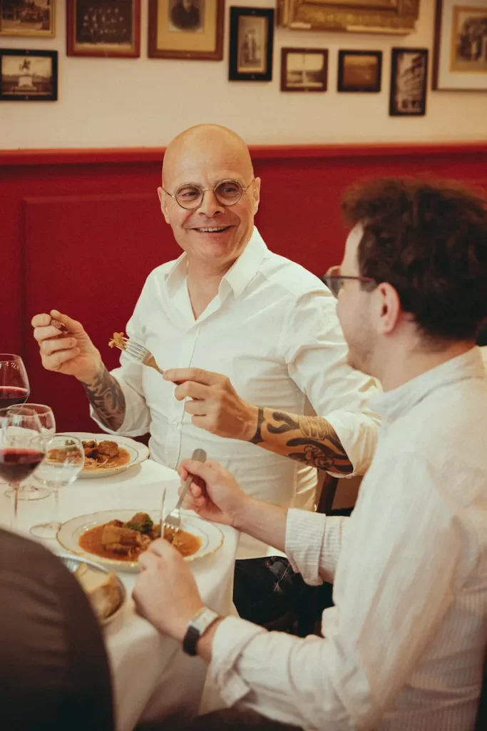 Deux convives qui rient en partageant un plat mijoté sous les photos anciennes de la salle du Bistrot Marie